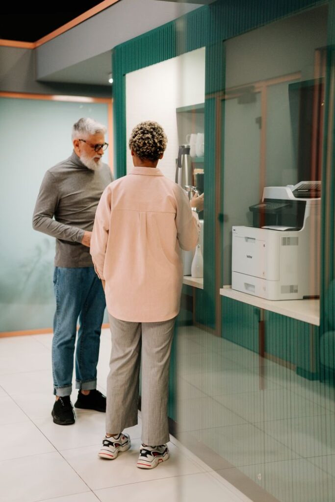 Two colleagues conversing during a coffee break in an office lobby with modern decor.